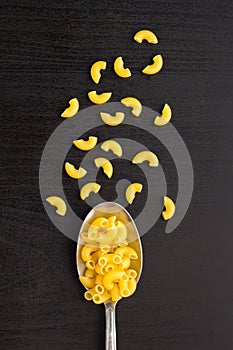 italian raw pasta horns dry on a metallic spoon and an black table