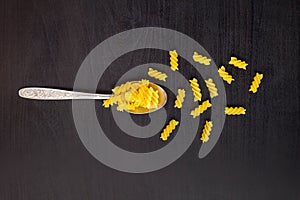 italian raw pasta spiral fusilli dry on a metallic spoon and an black table