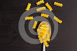 italian raw pasta spiral fusilli dry on a metallic spoon and an black table