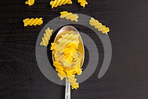 italian raw pasta spiral fusilli dry on a metallic spoon and an black table