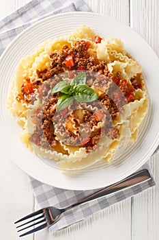 Italian Reginette pasta with bolognese sauce closeup on the plate on the wooden table. Vertical top view