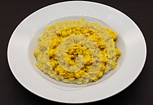 Italian Risotto allo Zafferano rice with saffron in a white dish isolated on black background