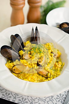 Italian risotto with saffron and seafood mussels on a white plate, vertical