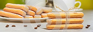 Italian savoiardi biscuits or ladyfingers cookies on a plate and in a stack, a jug of milk in the background