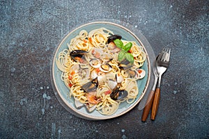 Italian seafood pasta spaghetti with mussels, shrimps, clams in tomato sauce with green basil on plate on rustic blue