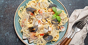 Italian seafood pasta spaghetti with mussels, shrimps, clams in tomato sauce with green basil on plate on rustic blue