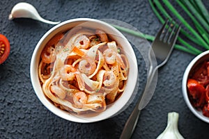 Italian tagliatelle pasta with shrimps and tomato sauce on dark background.