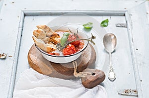 Italian tomato, garlic and basil soup Pappa al Pomodoro in metal bowl with bread on rustic wooden board over light blue