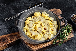 Italian tortellini pasta with cheese sauce in a pan. Black background. Top view