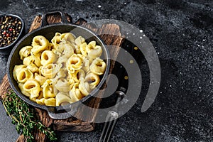 Italian tortellini pasta with cheese sauce in a pan. Black background. Top view. Copy space