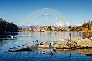 Italian town on the side of a river with mountains in the background, a swan on the water and a sunken boat