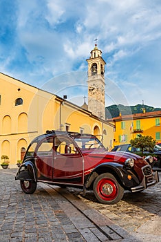 Italian town square with parked retro vintage car, church and colorful buildings in Lenno comune on Como lake, Lombardy