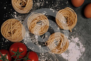 Italian traditional raw pasta with basil, cherry tomatoes and egg on a black stone background.