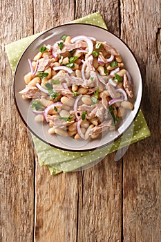 Italian traditional salad with tuna, onions and white beans close-up in a plate. vertical top view