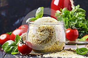 Italian uncooked pasta riso or orzo in a glass jar, tomatoes and