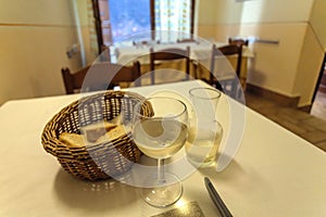 Italian white wine on table of traditional trattoria. Old restaurant interior with bread and drinks on table