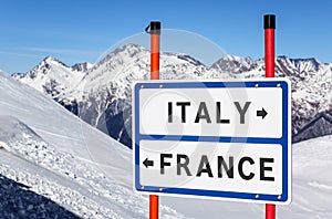 Italy or France choice to ski or snowboard. Information sign on winter mountain peaks under blue sky background