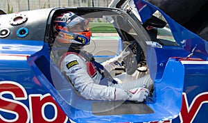 Driver in racing suit and helmet sitting in prototype race car cockpit