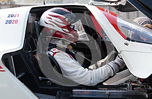 Driver in racing suit and helmet sitting in prototype race car cockpit