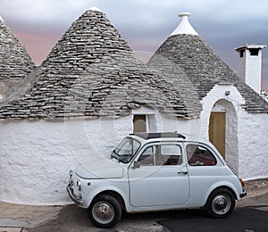 Italy. Traditional white washed trulli house with white Fiat vintage cinquecento 500 car parked in front, in Alberobello Puglia