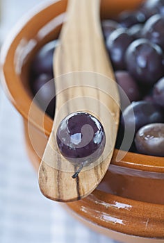 Italy, Tuscany, Magliano, Close up of black olives in bowl with one olive on wooden spatula