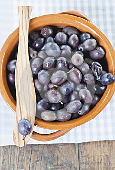 Italy, Tuscany, Magliano, Close up of black olives in bowl with one olive on wooden spatula