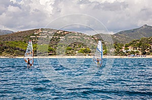 ITALY two man Windsurfing Sardinia on blue water in front of rocky coast