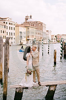 Italy wedding in Venice. The bride and groom are standing on a wooden pier for boats and gondolas, near the Striped