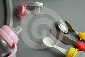 Items for feeding the baby. bottles, nipples, spoons and a knife on the grey table