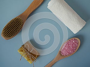 Items for spa treatments on a blue background, flat lay, top view. Sea salt bath, dry massage brush to maintain body