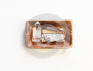 Items for spiritual cleansing - sage bundle, palo santo incense sticks and quartz crystal in wood tray