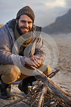 Itll get warm soon. A young man building a fire on the beach.