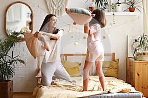 Its a battle. Excited happy older and younger sister fighting with pillows in bedroom, laughing and having fun together