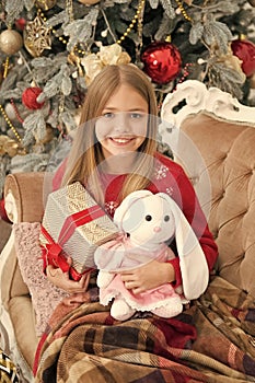 Its so cuddly and soft. Small child happy smiling with presents. Little girl with cute bunny at Christmas tree. Small