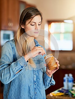 Its about enjoying the sweet things in life. a young woman eating peanut butter out of the jar with a spoon.