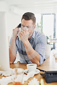 Its flu season. a young businessman blowing his nose while speaking on the phone in an office.