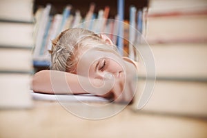 Its getting a bit too much for her. A cute young girl fast asleep while surrounded by books at the library.