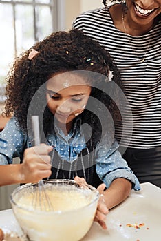 Its getting messy in the kitchen. a little girl baking at home with her mothers help.
