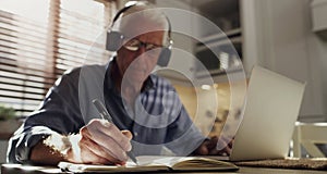 Its going to be a busy day. a senior man sitting alone in the kitchen and wearing a headset to work from home.