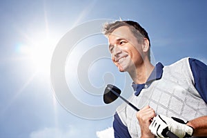 Its a great day for golf. Smiling mature man holding his golf club while against a blue sky - low angle.