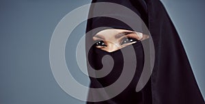 Its in her eyes. Studio shot of a young arabic woman wearing a burka against a gray background.