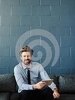 Its my little handheld office. Cropped portrait of a handsome young businessman using his digital tablet in the office.