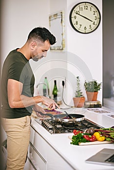 Its my turn to cook today. Cropped shot of a handsome young man cooking in the kitchen at home.