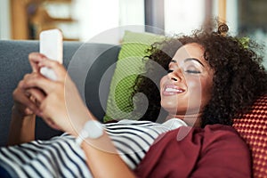 Its no the weekend until youre relaxing. a young woman using a mobile phone while relaxing on the sofa at home.