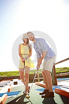 Its not as easy as it looks. A happy young couple playing putt-putt on a sunny day.