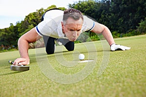 Its not cheating if nobody saw it. Shot of a handsome man trying to blow his golf ball into the hole.