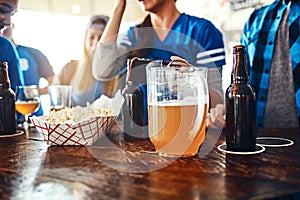 Its not a game without drinks and snacks. a jug of beer and popcorn on a counter at a sports bar.