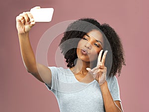 Its not a selfie until you pucker and pout. Studio shot of an attractive young woman taking a selfie against a pink