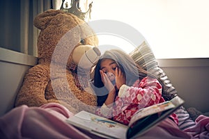 Its one of the most exciting stories shes read. an adorable little girl looking surprised while reading a book in bed.