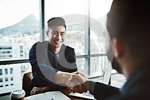 Its safe to say he made a great impression. Shot of two young businessmen shaking hands while sitting at a desk in a